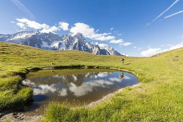 Hiker with dog admires the peaks of Mont De La Saxe reflected in water, Courmayeur