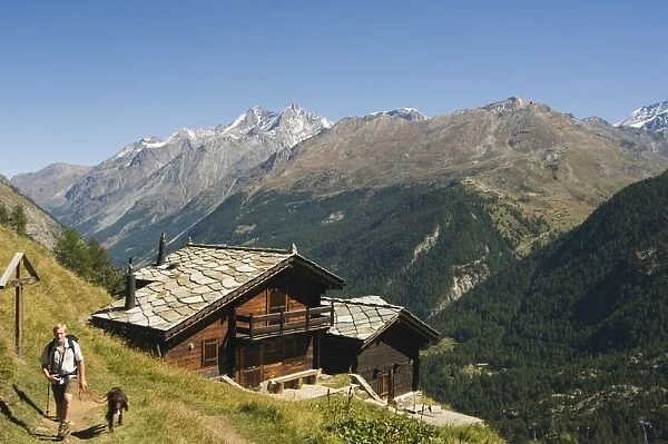 Hiker and dog on trail in front of traditional slate roofed house