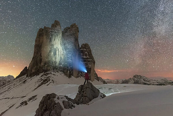 Hiker with head torch views the Tre Cime di Lavaredo on a starry night with the Milky Way, winter view, Tre Cime di Lavaredo (Lavaredo peaks), Sesto (Sexten), Dolomites, South Tyrol, Italy, Europe