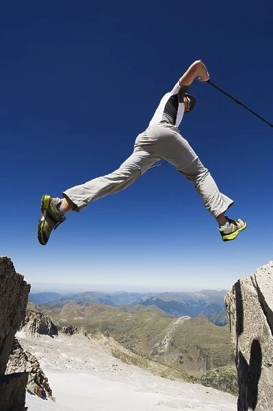 Hiker jumping across a gap in the rocks, Pico de Aneto, the highest peak in the Pyrenees