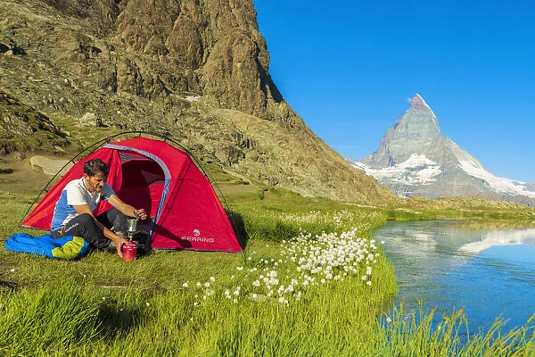Hiker at lake Riffelsee makes coffee out of the tent facing Matterhorn, Zermatt, canton of Valais