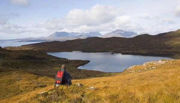 Hiker looking across Loch Dhughaill towards the distant Cuillin Hills, Sleat Peninsula