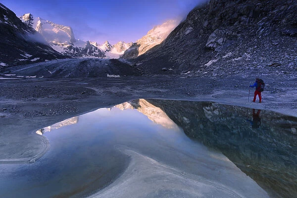 Hiker looks at sunrise from a pond at Forno Glacier, Forno Valley, Maloja Pass, Engadine