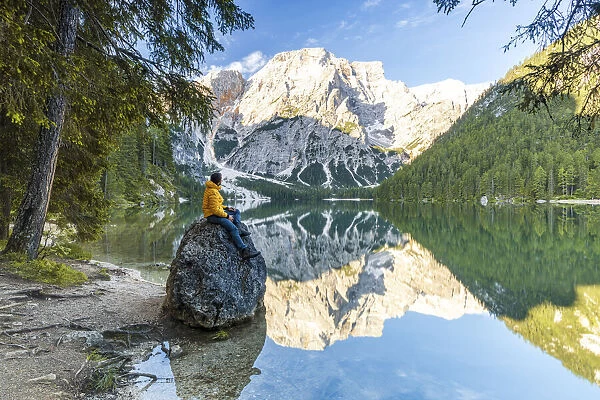 Hiker man enjoying sunrise sitting on rocks on shore of Lake Braies (Pragser Wildsee