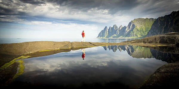 Hiker man walking on waters edge admiring mountains reflected in the sea, Tungeneset