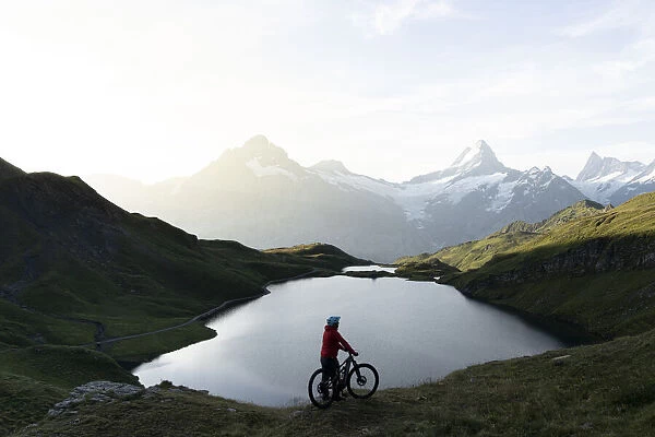 Hiker with mountain bike admiring sunrise over Bachalpsee lake, Grindelwald