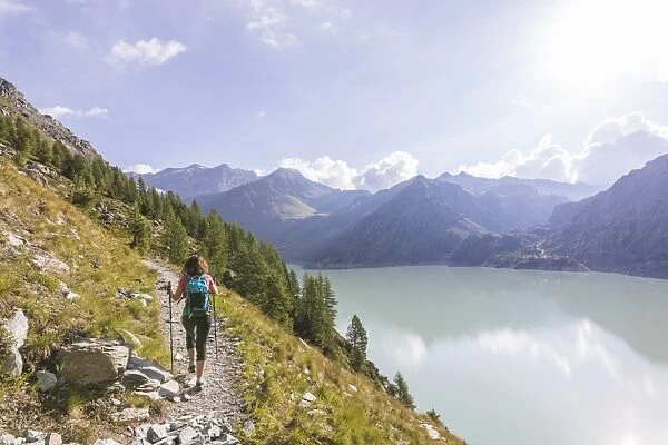 Hiker on path towards Rifugio Bignami beside the dam and water basin of Alpe Gera