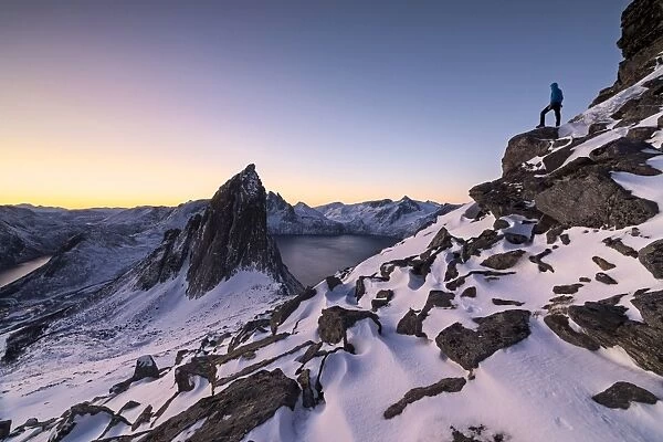 Hiker on peak Hesten admires Mount Segla and the Mefjorden framed by frozen sea at sunrise