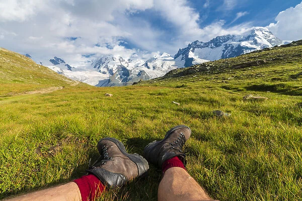 Hiker rests on grass looking towards Monte Rosa massif, Riffelalp, Zermatt, canton of Valais