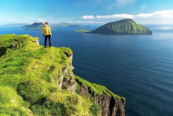 Hiker stands on top of a cliff admiring the rugged view, Nordradalur, Streymoy island, Faroe islands, Denmark, Europe