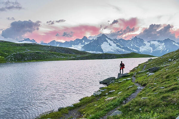 Hiker stands near the shore of Fenetre lake admiring the sunset over the massif of Mount Blanc, Ferret valley, Valais canton, Col du Grand-Saint-Bernard (St. Bernard mountain pass), Switzerland, Europe