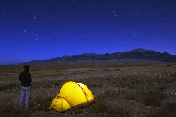Hiker and tent illuminated under the night sky, Great Sand Dunes National Park