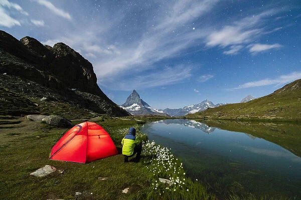 Hiker out of tent looks towards Matterhorn from lake Riffelsee, Zermatt, canton of Valais