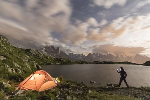 Hiker and tent on the shore of Lacs De Cheserys at night with Mont Blanc massif in background