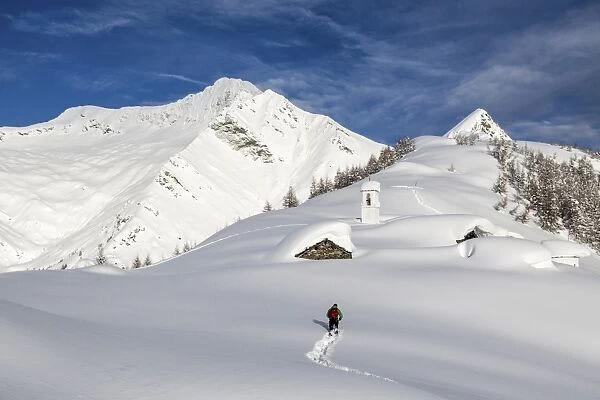 A hiker trying to approach the little village at the Scima Alp covered in snow, Valchiavenna, Lombardy, Italy, Europe