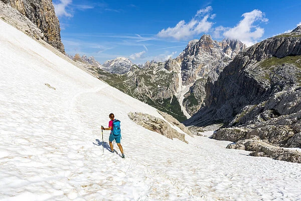 Hiker woman walking on snowy mountain ridge on path to Rifugio Locatelli hut