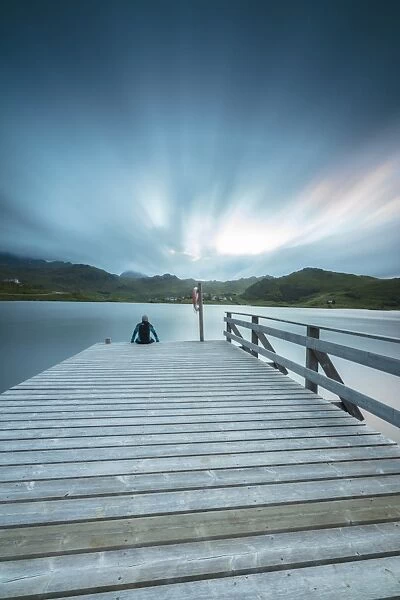 Hiker on wooden deck admires the sea illuminated by blue lights at night, Holdalsvatnet