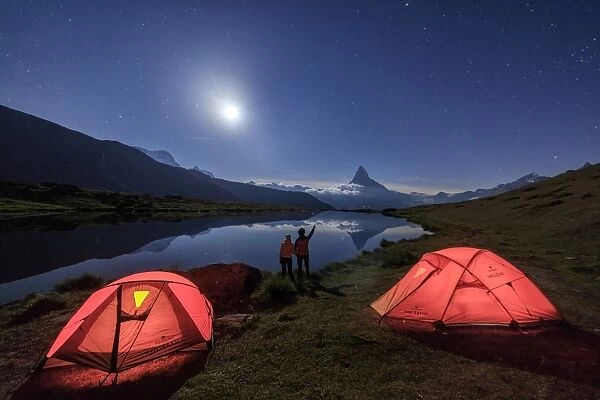 Hikers admire Matterhorn reflected in Lake Stellisee on a starry night of full moon