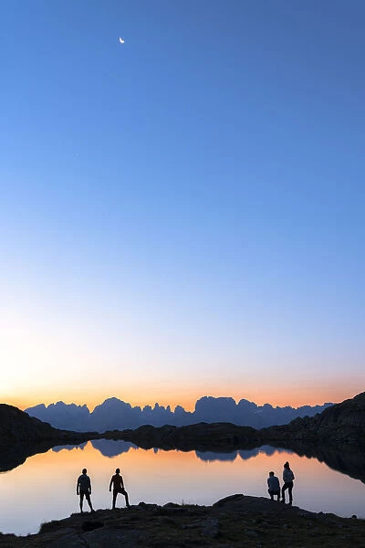 Hikers admiring Brenta Group Dolomites reflected in Lago Nero di Cornisello at dawn