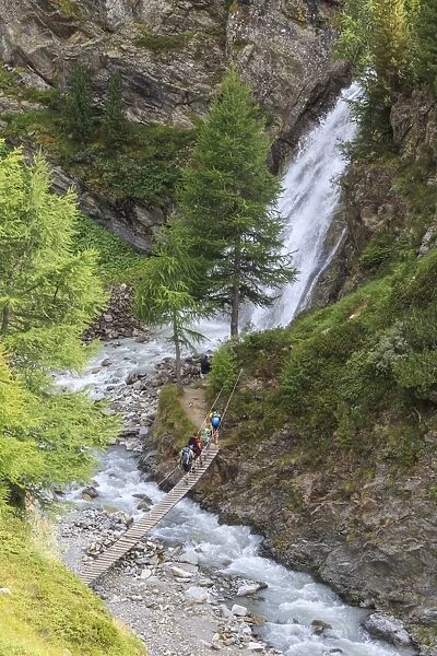 Hikers cross the wooden bridge on a creek in the woods, Minor Valley, High Valtellina