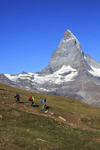Hikers proceed with the Matterhorn in background in a clear summer day, Gornergrat
