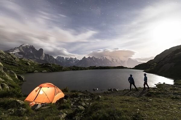 Hikers and tent on the shore of Lacs De Cheserys at night with Mont Blanc massif in the background