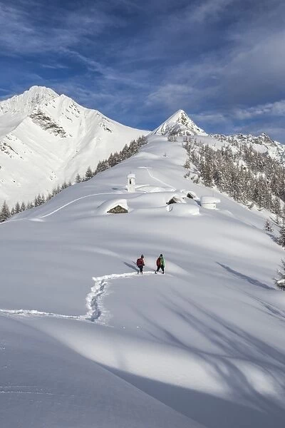 Hikers trying to approach the little village at the Scima Alp covered in snow, Valchiavenna, Lombardy, Italy, Europe