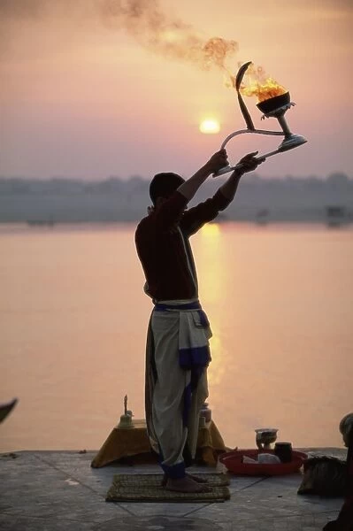 Hindu man worshipping in front of setting sun