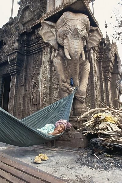 Homeless woman in a hammock attached to an elephant carving in a central temple in Phnom Penh