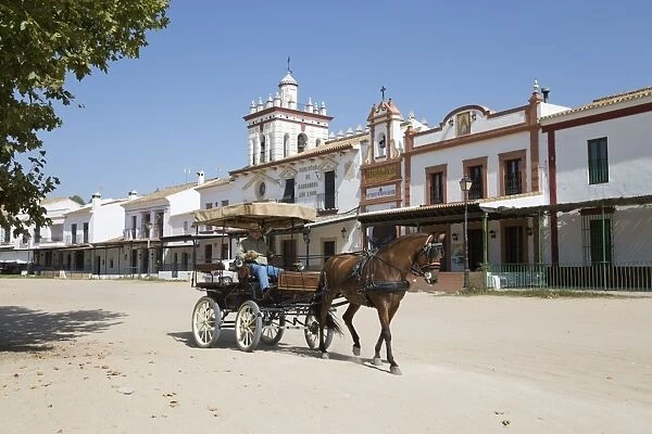 Horse and carriage riding along sand streets with brotherhood houses behind, El Rocio