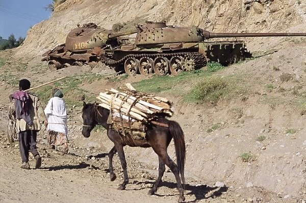 Horse carrying wood passes rusting tank from the war, Sentebe, Choa region