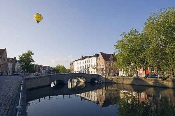 Hot air balloon floating over rooftops, houses reflected in a canal, old town