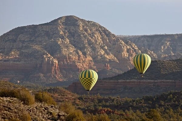 Two hot-air balloons flying low among red rock formations, Coconino National Forest