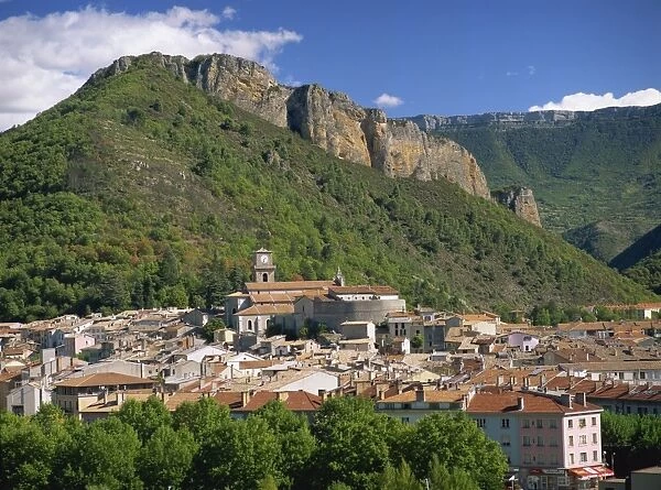 Houses and church with bell tower below a rocky hill at Digne les Bains