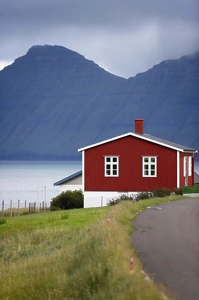 Houses at Hellur, small village near Oyndarfjordur, cliffs of Kalsoy Island in background