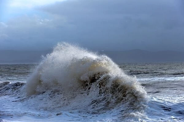 Huge waves crash against a stone jetty at Criccieth, Gwynedd, Wales, United Kingdom