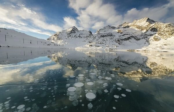 Ice bubbles frame the snowy peaks reflected in Lago Bianco, Bernina Pass, canton of Graubunden