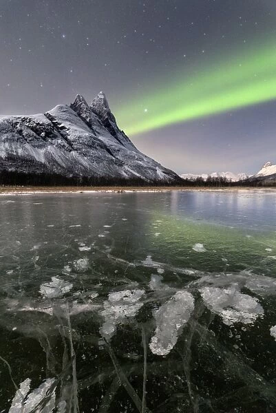 Ice bubbles of frozen sea and the snowy peak of Otertinden under the Northern Lights