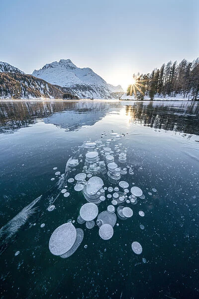 Ice bubbles trapped in frozen Lake Sils at sunset with Piz Da La Margna in background