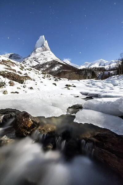 Ice on rocks frames the granitic snowy peak of the Stetind mountain under the starry sky