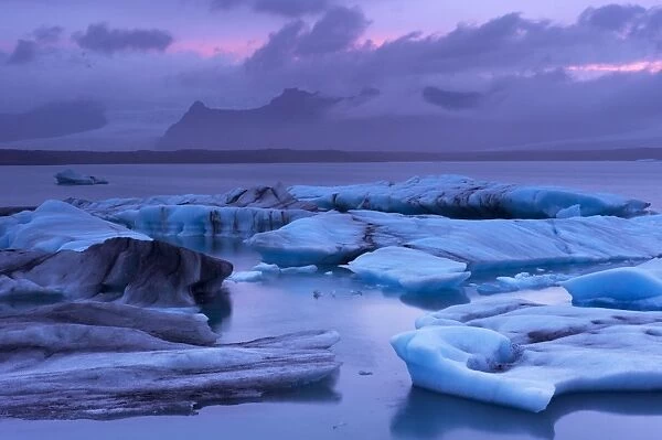 Icebergs in Jokulsarlon glacial lagoon, at dusk, Oraefajokull (Vatnajokull) glacier in the distance