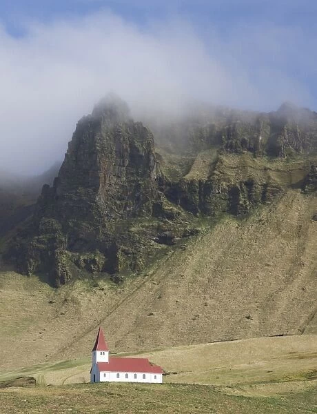 Icelandic church dwarfed by mountains rising into mist, Vik i Myrdal, South Iceland