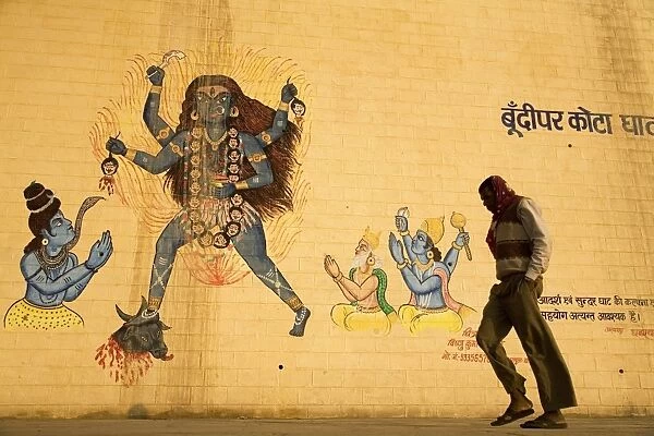 An Indian man walks by a wall painted with images of Hindu deities in Varanasi