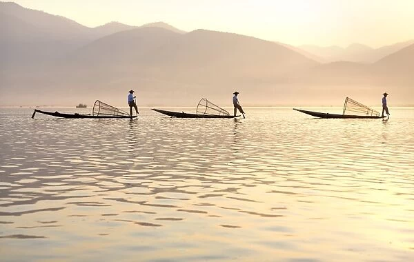 Intha leg rowing fishermen at sunset on Inle Lake who row traditional wooden boats using their leg and fish using nets stretched over conical bamboo frames, Inle Lake, Myanmar (Burma), Southeast Asia