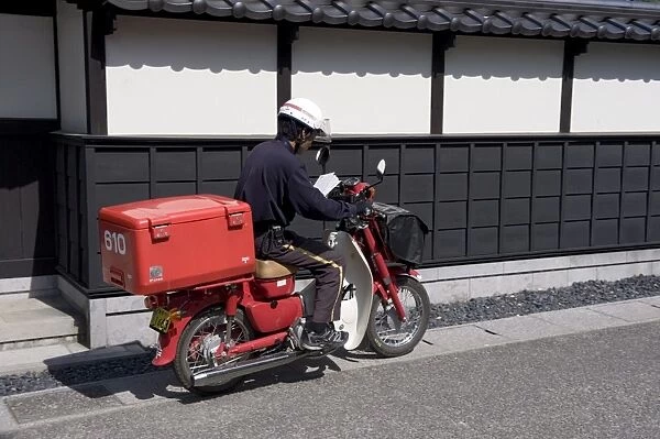 A Japanese postman riding a typical red scooter making his rounds, Japan, Asia