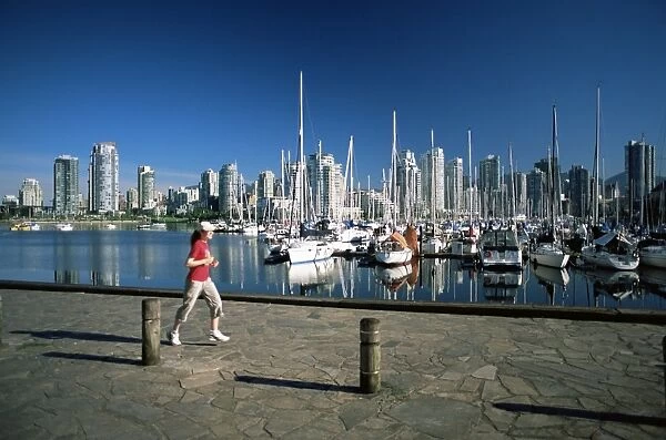 Jogger passing in front of False Creek marina, with downtown skyscrapers behind