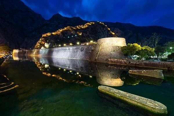 Part of Kotors old town wall and lit fortress ramparts reflected during the evening blue hour