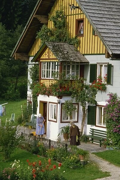 Two ladies outside a typical house with summer flowers in windowboxes and in the garden