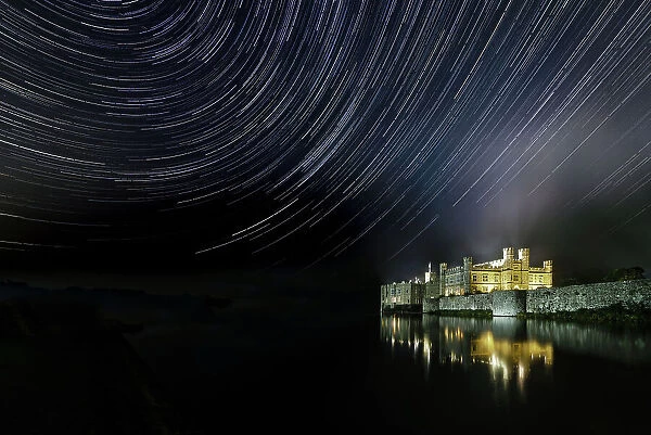 Leeds castle illuminated reflected in moat showing star trails in the night sky, near Maidstone, Kent, England, United Kingdom, Europe