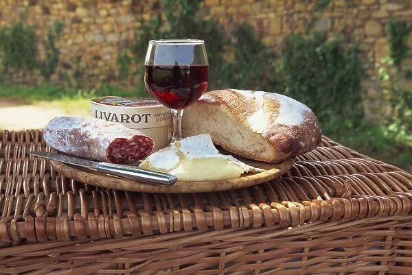 Still life of bread, cheese, glass of red wine and sausage, picnic lunch on top of a wicker basket